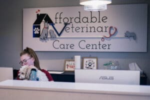 receptionist sitting behind desk with affordable veterinary care center logo on wall in background